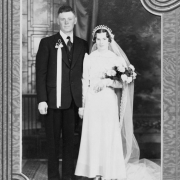 Wedding portrait of Mr. and Mrs. Grasmich, Ordway, Crowley County, Colorado. The bride wears a gown with veil and bouquet; the groom wears a suit with a ribboned boutonniere.
