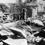 Remains of First National Bank, 4th (Fourth) street and Bennett Avenue, Cripple Creek, Colorado, after first fire on April 25, 1896; men on  wooden plankway inspect remains of brick vault; twisted corrugated metal and chain link fence (possibly original tellers cage) illustrate the devastation from the fire.