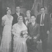 Studio portrait of the Edwardo Lopez and Ida Chavez Lopez wedding party, Denver, Colorado. They are identified (left to right) back row:  unknown woman, Manuel Moya, Racheal Chavez Moya, and Tony Lopez. Front row: Edwardo Lopez and his bride Ida Chavez Lopez. Ida wears a silk and lace wedding gown a lace veil and holds a bouquet of roses. Edwardo wears a suit and has a boutonniére. Racheal Chavez Moya wears a hat.