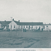 View of Colorado Senator Casimiro Barela's country home  in El Moro (Las Animas County), Colorado. Shows a house with gabled roofs and an small cabin. Men and women pose near the house and near horse drawn carriages. Senator Barela poses right center with an unidentified woman.
