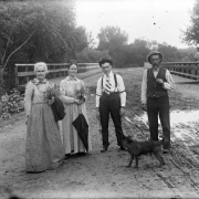 Outdoor portrait of two couples on Alameda Avenue in Denver, Colorado. The women hold bouquets of flowers. One man wears suspenders and an armband. A dog and the Alameda Avenue bridge over the South Platte River are nearby.