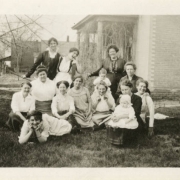 Photograph of a group of several unidentified woman outside of a house in the Elyria-Swansea neighborhood of Denver, Colorado.  Most of the women sit on the ground, a few stand behind them.  One woman holds a small baby on her lap, while another small child stands behind them watching.
