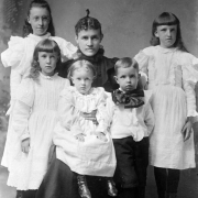 A mother in a dark dress poses for a family portrait with her five young children, Silver Plume, Clear Creek County, Colorado. Four of the children are girls in light colored dresses, one is a boy with a light colored shirt, dark pants, and a large bow-tie.
