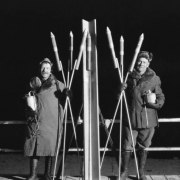 Members Garrett and MacDonald of the AdAmAn Club pose with fireworks including rockets and bombs with fuses, on top of Pikes Peak, Colorado Springs, El Paso County, Colorado. They wear tall lace-up boots and fur collared parkas.