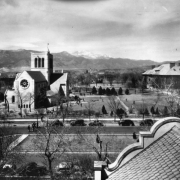 View of Colorado College, Colorado Springs, El Paso County, Colorado, from the Lennox house roof; shows Shove Memorial Chapel (gift of Eugene P. Shove). John Gray's design includes a square belltower, turret, and rosette window. Cars line Nevada Avenue; Palmer Hall edges lawn.