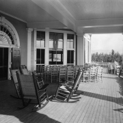 Deck and rocking chairs are arranged on the balcony of the Casino at the Broadmoor Hotel and Casino, Colorado Springs, El Paso County, Colorado. A fanlight tops double doors; columns with ornate capitals support the beamed ceiling.