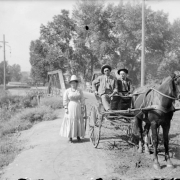 Outdoor portrait of people and a horse drawn buggy by the wood suspension bridge over Archer Canal in Denver, Colorado; the Alameda Avenue bridge is in the background.
