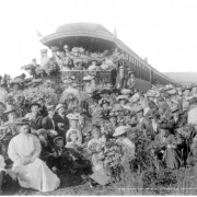 View of large group of men, women & children holding bouquets of wildflowers posed behind Colorado Midland Railway passenger train, somewhere in Colorado; observation car number 111 preserved at Colorado Railroad Museum in Golden, Colorado; wildflower excursion train; copy glass plate attributed to L.C.McClure.