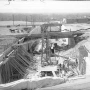 View of Alameda underpass construction in Denver, Colorado; shows concrete forms, railroad bridges, machinery, sheds, and men working.