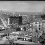 Right center of panorama view taken from Colorado State Capitol Building, Denver, Colorado; includes downtown business district with. Signs read: "Plymouth Hotel," "Tours," " Overland Auto Co.," "The Byron Motor Car Co.," "F. C. Ayres, Fireproof Grain Elevator," The Front Range with snow covered Longs Peak is in the distance.
