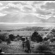 Evening view of Mount Princeton and Buena Vista (Chaffee County), Colorado; thought to be L.C. McClure standing behind camera & tripod; box of camera supplies, foreground left; Collegiate Range, Rocky Mountains, and dramatic clouds.