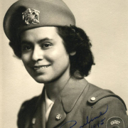 Studio bust portrait of Pauline Apodaca, a member of the United States Cadet Nurse Corps. She wears a uniform with brass buttons and a sleeve patch that reads: "Cadet Nurse" and a beret with a metal insignia.