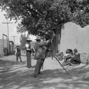 View of a photographer with tripod and camera, and his subjects, Native American men, women and children, in Taos, New Mexico.