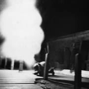 A member of the AdAmAn Club squats down and looks away as fireworks illuminate the area outside the Cog Railway Terminal building, Pikes Peak, Colorado Springs, El Paso County, Colorado.