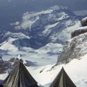 View of Camp Two looking through Cadaver Gap at Camp Muir, (also known as Camp One during the Mount Rainier Test Expedition conducted by men from the 87th Mountain Infantry Regiment, re-enforced). Two pyramid tents are pitched in the snow in the foreground. The stone cabin at Camp Muir is visible on a slight rise across a large open snow field. Beyond Camp Muir rough mountain territory stretches into the distance.