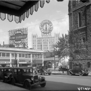 View, from Broadway and 18th (Eighteenth) Street, of the Continental Oil building at 17th (Seventeenth) Street and Glenarm Place in Denver, Colorado. Automobiles line the street near Trinity Methodist Church. Signs read: "Conoco Products", "Chevrolet", "Sightseeing Office", "City Trip $1.00", "Lookout Mtn. $2.50", "Rocky Mountain Cleaners And Tailors Phone Champa 3035-W", "Photo-engravers Artists Burke-McMillin Engraving Co. Illustrators Designers", "Marion Cafe", and "Au-to Shades".
