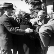 President Franklin D. Roosevelt leans out of his touring car, during his campaign visit to Denver in 1936, to talk with a supporter. Four other men stand nearby.