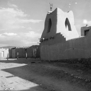 View of Taos Pueblo, New Mexico; shows Native American (Taos Pueblo) adobe walls, a tower with arches, and a lamp.