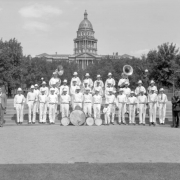 The Alamosa Shop Employees Band of the Denver & Rio Grande Western Railroad poses in three rows, in front of State Capitol, Civic Center, Denver, Colorado. Each wears a uniform and holds an instrument. Standard-bearers hold the American flag and the band's standard with railroad logo and "Alamosa" printed on it.