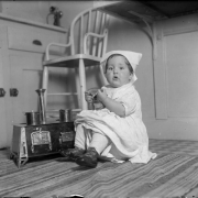 Harriet Rhoads, daughter of Harry M. Rhoads plays in the kitchen with her toy pots and stove, Denver, Colorado. Shows: cabinets, chair, rug.