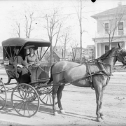 View of a horse, buggy, man and woman, in (probably) Denver, Colorado. Frame residences are in the background.