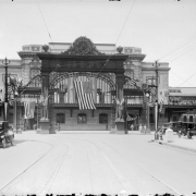 View of the Mizpah Arch and Union Station in Denver, Colorado. United States flags hang over 16th (Sixteenth) Street and parked cars.