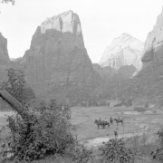 View of people riding horses on the valley floor between towering  cliffs at Zion National Park, Utah.