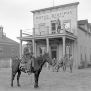 View of a hotel in Kanab, Kane County, Utah; shows a man on horseback with an axe, men on the porch or balcony of the frame structure, and lettering: "Hotel Highway W. S. Rust, Proprietor."