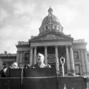 United States President Franklin Delano Roosevelt speaks from a podium in Denver, Colorado. The Colorado State Capitol portico and dome are in the background.