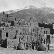 View of Taos Pueblo, New Mexico; shows adobe pueblo dwellings, hornos (bee-hive ovens), Pueblo Peak, and Native Americans (Taos).
