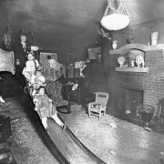 Interior view of a living room at the Gates' home in Denver, Colorado with (probably)  Hazel Gates and her three daughters on a slide. Shows: fireplace, lamps, and a child's wicker chair.