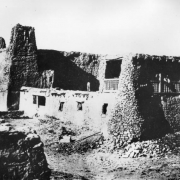 View of the old mission church and convent at the Native American, Acoma Pueblo, show a few men posing on balconies of the weathered adobe structure.