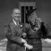 Newlyweds Helen Bonfils and George Somnes pose outside of a home. Helen wears a corsage, hat and string of pearls. The pearls may have been a gift given to her by Mrs. Harry H. Tammen, the hostess of the newlyweds wedding breakfast. George Somnes wears a suit, tie and a flower pinned on his lapel. Helen and George were married on September 15, 1936.