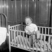 A small boy cries, climbing the side of his crib.
