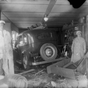 A man and woman pose by an automobile, wreckage, and interior store walls.