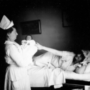 Mrs. Charles (Hazel LaDora Rhoads) Gates and her newborn baby in Denver, Colorado; a nurse holds the baby next to the bed.