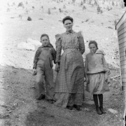 A woman in a gingham dress with puffed shoulders poses with a boy and girl, probably in Colorado.