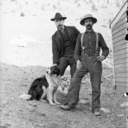 Men pose with a dog; clothing includes hats and suspenders; one man smokes a pipe, probably in Colorado.