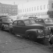View of automobiles on Welton Street in Denver, Colorado. Background signs read: "Rock Island Lines, Route of the Rockets," "Hotel Denver, 80 Outside Rooms, $1.00 to $3.00, Thoroughly Modern, Permanent and Transient."