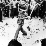 A boy in a blindfold swings a stick at a pinata in Denver, Colorado; Chicano boys and girls look on.