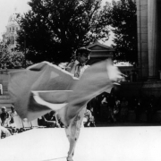 A Mexican-American man dances at Civic Center, in Denver, Colorado; he wears a bullfighter costume and twirls a cape. People look on.