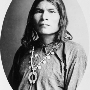 Studio portrait of a Native American (Navajo) man. The man wears a shirt and a squash blossom necklace.