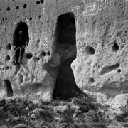 Man sits in a window opening of a Native American (Tewa) talus dwelling at the Puye Cliff Dwellings, Santa Clara Pueblo, New Mexico. The talus dwellings have holes for vigas and petroglyphs on the exterior wall.