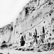A man stands on a wooden ladder at the Long House Ruin, Native American (Anasazi) talus dwelling, Bandelier National Monument, New Mexico. Other ladders lean against the tuff dwellings which have holes for vigas.