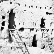 Close-up view of Native American (Anasazi) talus dwellings at Bandelier National Monument, New Mexico. Two ladders rest against irregularly shaped door openings. The tuff dwellings have holes for vigas.