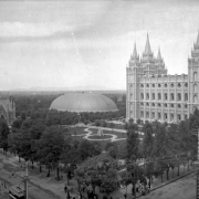 View, facing northwest at the corner of Main and South Temple Streets, of Temple Square, in Salt Lake City, Utah. The Temple of the Church of Jesus Christ of Latter-Day Saints, the Mormon Tabernacle, the Seagull Monument, and Assembly Hall (Endowment House) are in view. A gold statue of Moroni on the main spire of the temple is visible. A trolley car, tracks, and electrical wires are on and above South Temple Street.