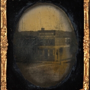 View of a building probably in Denver, Colorado. Signs on the buildings read: "Miller's New Drug Store" and "Dry Goods Groceries".