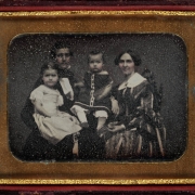Shows Hiram and Alida Burton with their children Elsie and Smith Payne Burton. Two young children sit on the lap of the man. The young girl wears a dress, and the toddler wears a pullover with bloomers. The woman wears a dress with a lace collar and the man wears a suit.