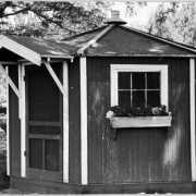 View of the octagonal lawn bowling office in Washington Park, Denver, Colorado. The wood panel building has a window box and covered entrance.