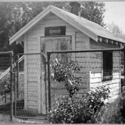 View of a wooden building surrounded by a wire fence at Berkeley Park in Denver, Colorado. A wood cart is supported by the fence. A sign on the building reads: "Danger".